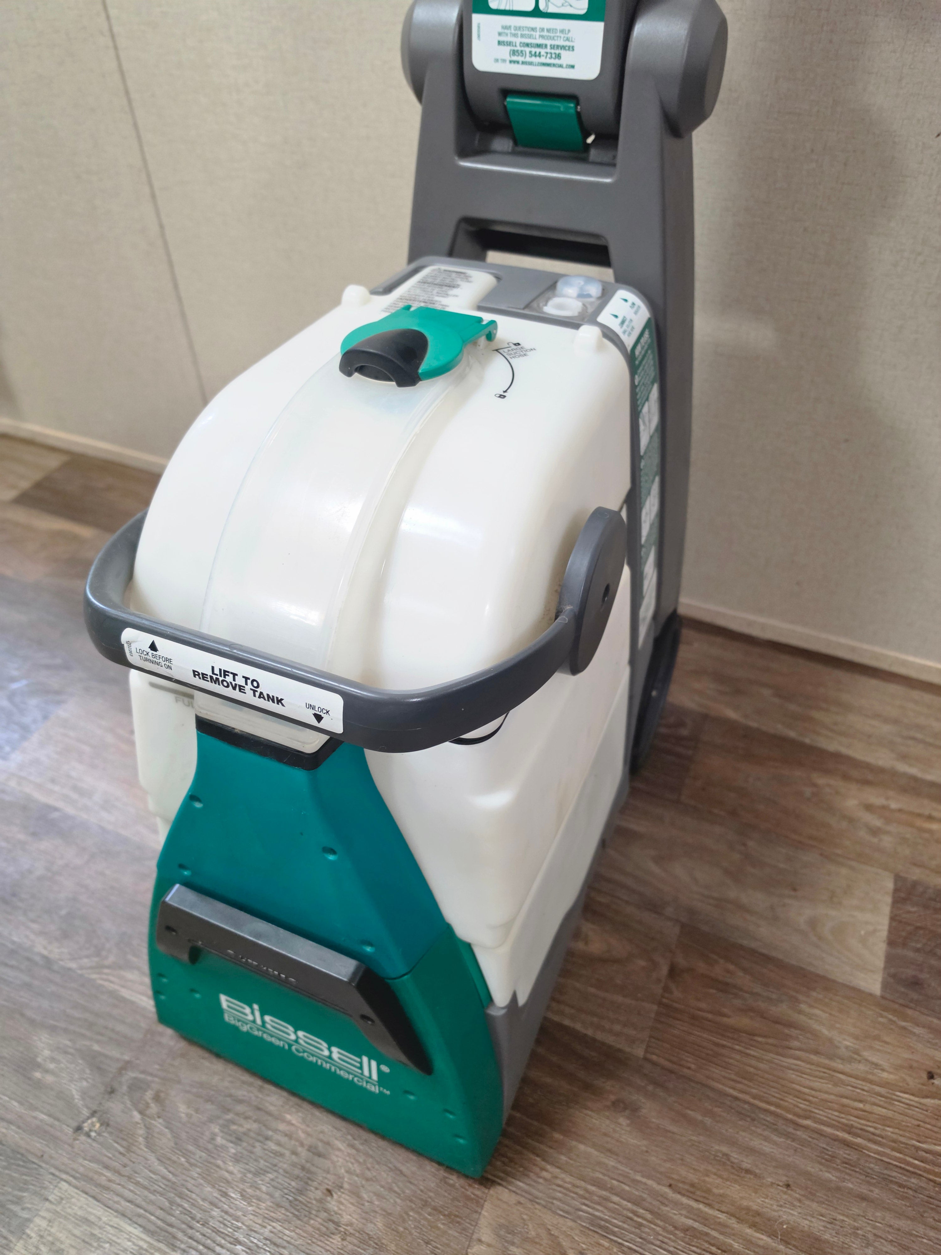 Front-right angled close-up of the BISSELL BigGreen base, clear recovery tank, and green handle latch.