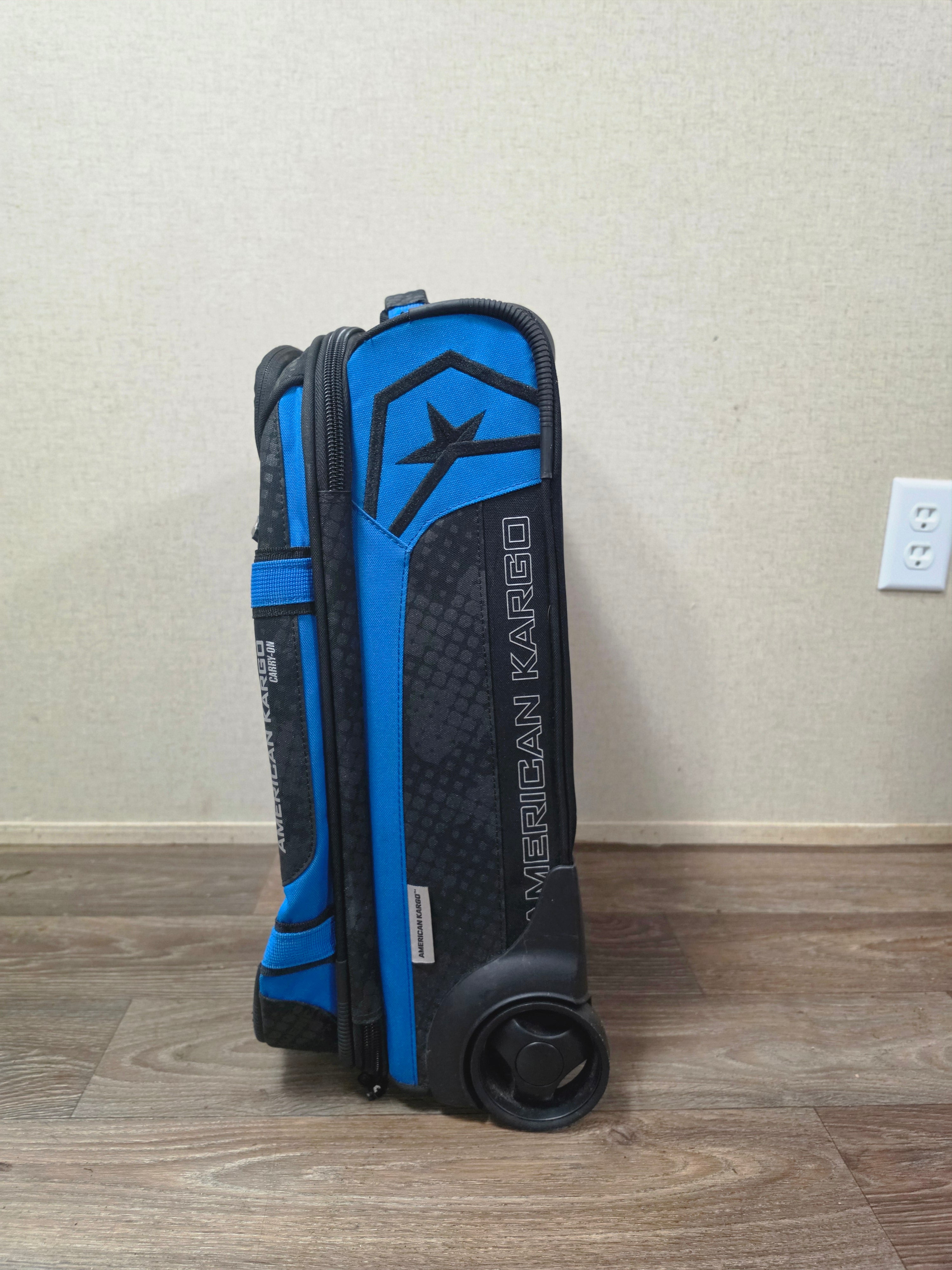Side profile of the black and blue American Kargo bag showing a wheel and branded panel.