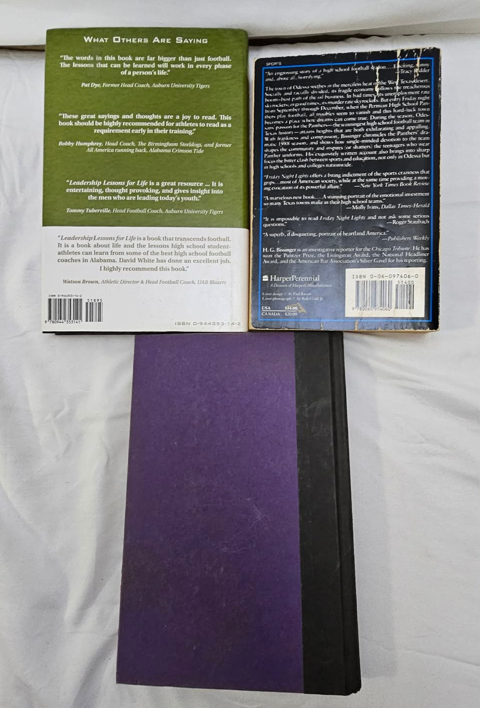 Back covers of two football books displayed above black and purple hardcover books.
