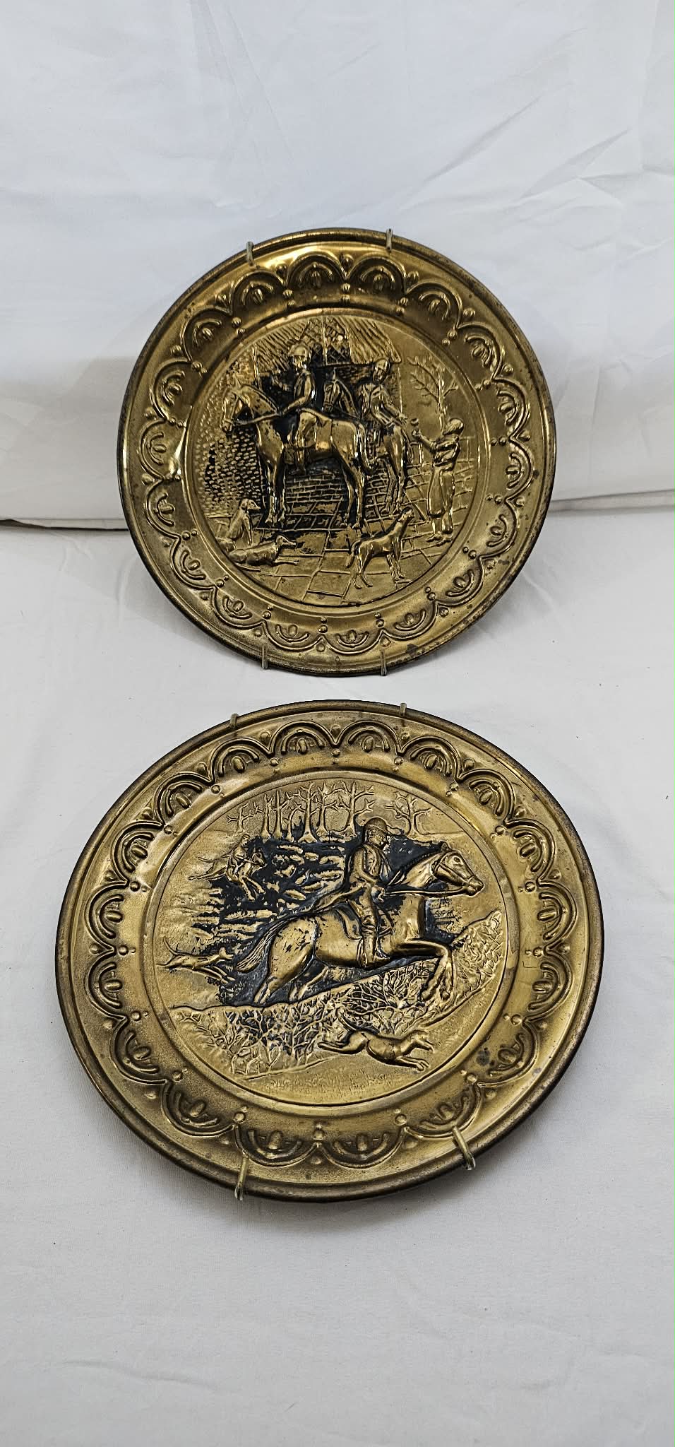 Alternate front view of two vintage brass-tone English hunting-scene wall plates displayed together.