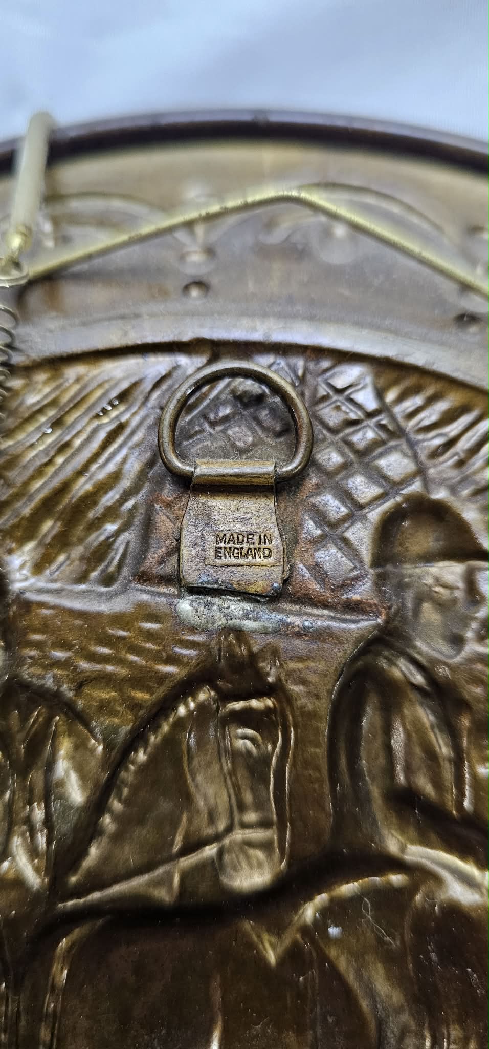 Close-up of the Made in England mark and hanger attachment on the back of a vintage brass-tone hunting-scene wall plate.