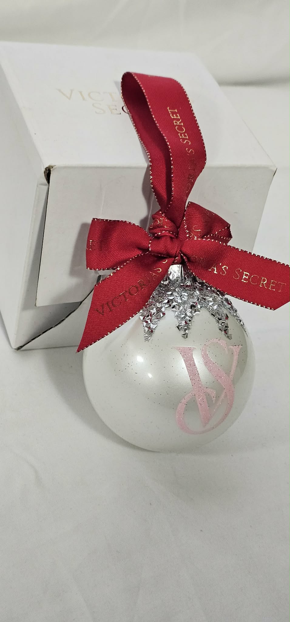 Angled view of Victoria's Secret white glass ornament with branded burgundy ribbon and box